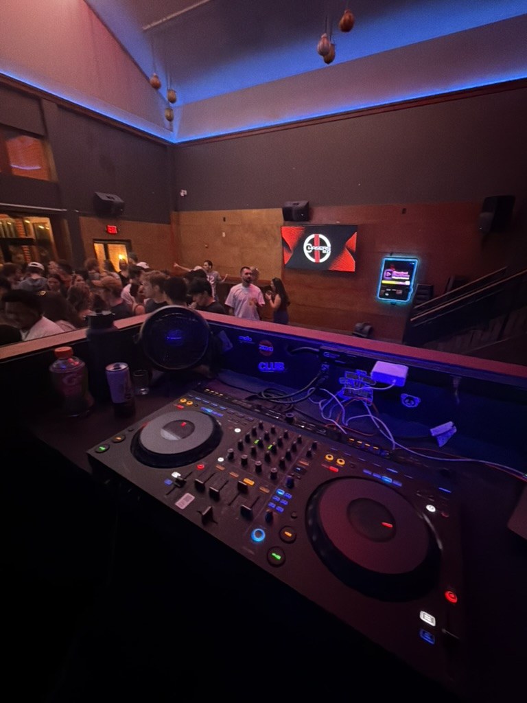 The view from the DJ booth at Chasers: decks in the foreground, a packed room beyond